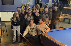 A group of students all grouped up for a photo infront of a pool table.